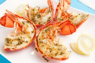 cooked lobster tails split open on table with spices and herbs
