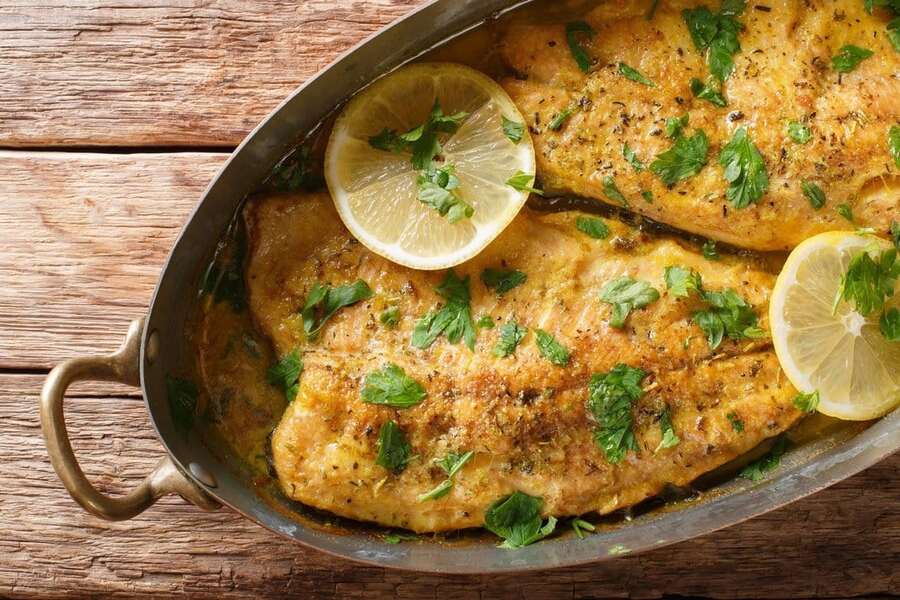two cooked new england haddock fillets with herbs and lemon in a pan