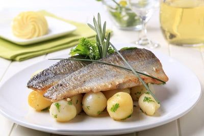 two cooked rainbow trout fillets over a bed of potatoes with herbs