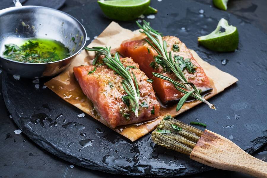 two cooked wild alaska coho salmon portions with herbs and lime on a black plate