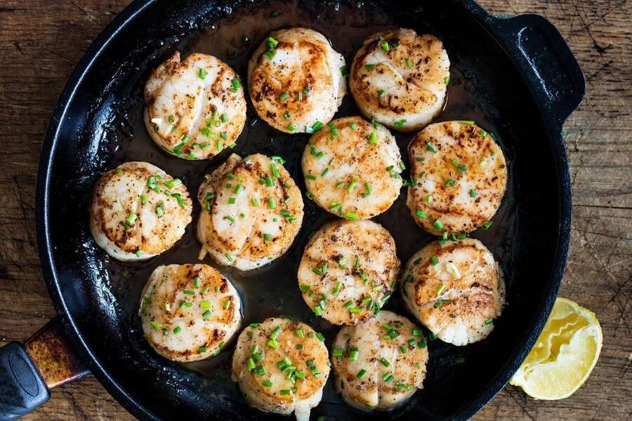 cooked wild sea scallops with herbs in a pan