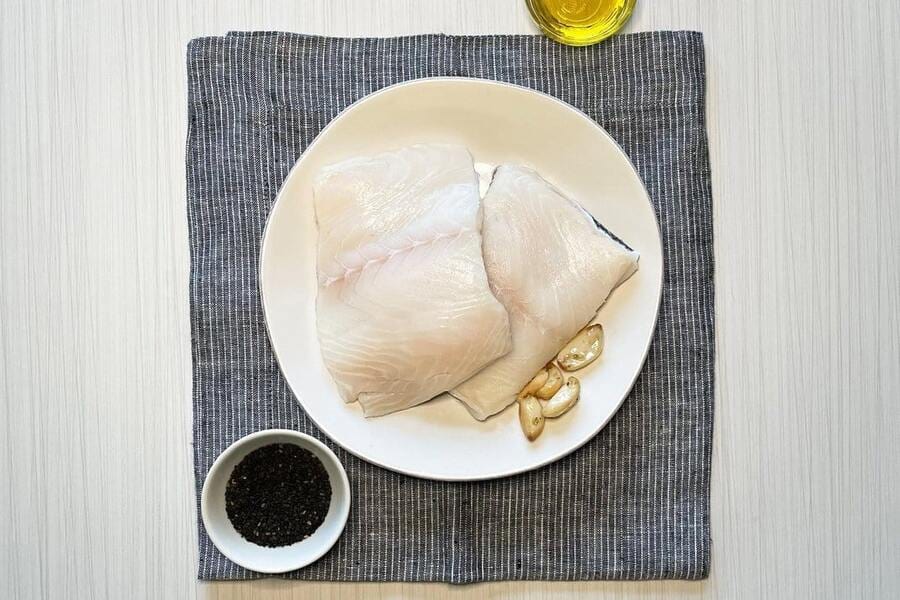 two raw wild alaska black cod portions on a white plate with spices