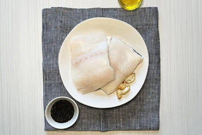 two raw wild alaska black cod portions on a white plate with spices