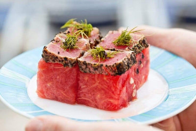 four raw yellowfin tuna saku squares topped with seared tuna saku pieces and herbs on top