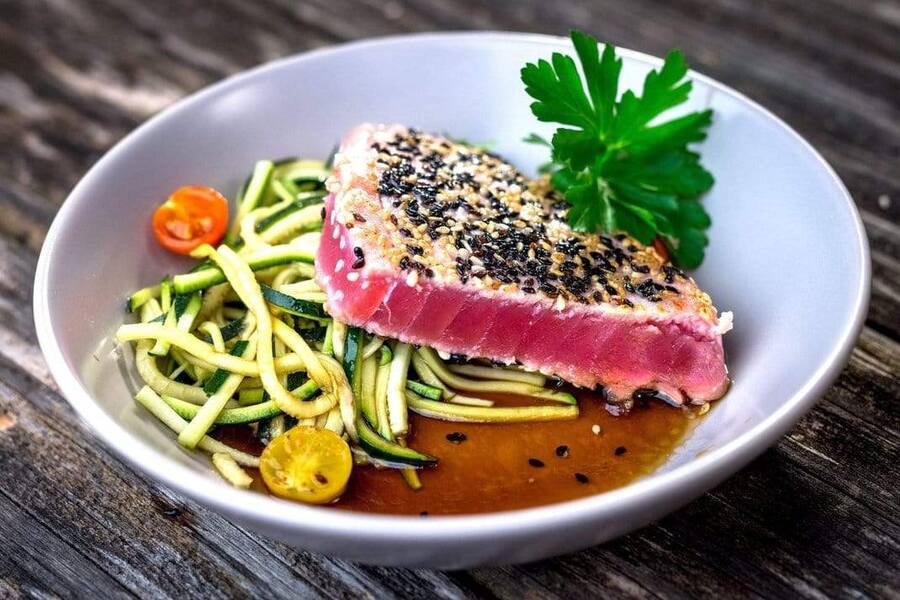 pan seared yellowfin tuna steak with sesame seed crust in a bowl over soy sauce and veggies