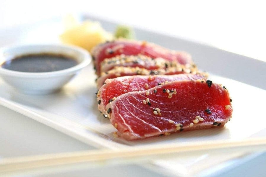 seared yellowfin tuna steak pieces with sesame seeds on a white plate with soy sauce