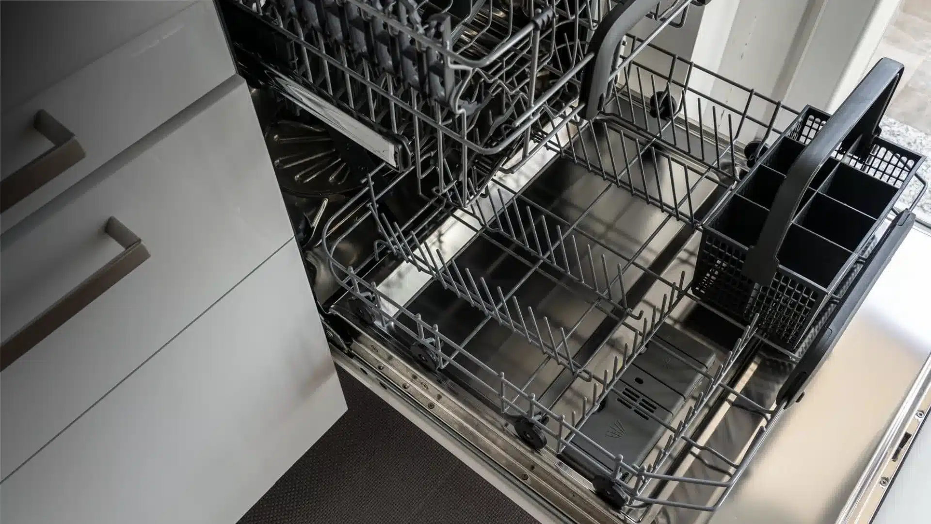 An image for how to clean dishwasher showing an empty, clean dishwasher next to white cabinets with silver handles