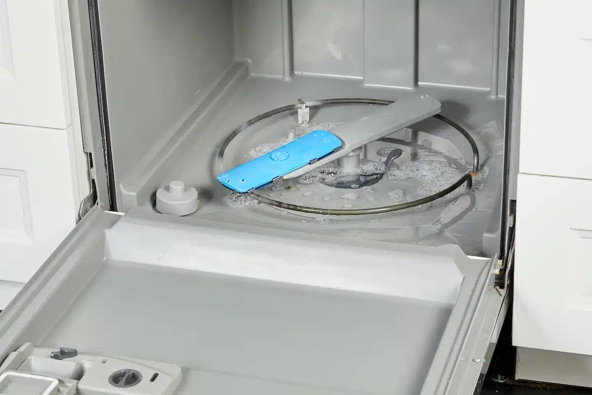 An image showing how to clean dishwasher, where the interior of an empty stainless steel dishwasher is seen without any racks