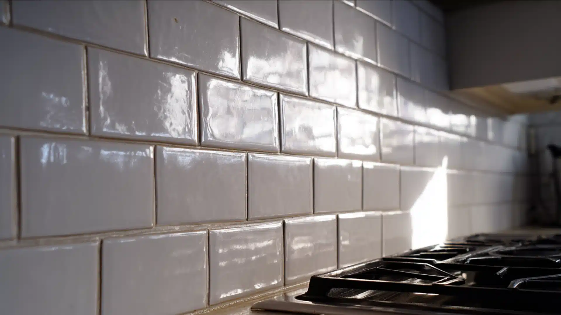 shiny white subway tiles reflect sunlight above a black stovetop in a kitchen space
