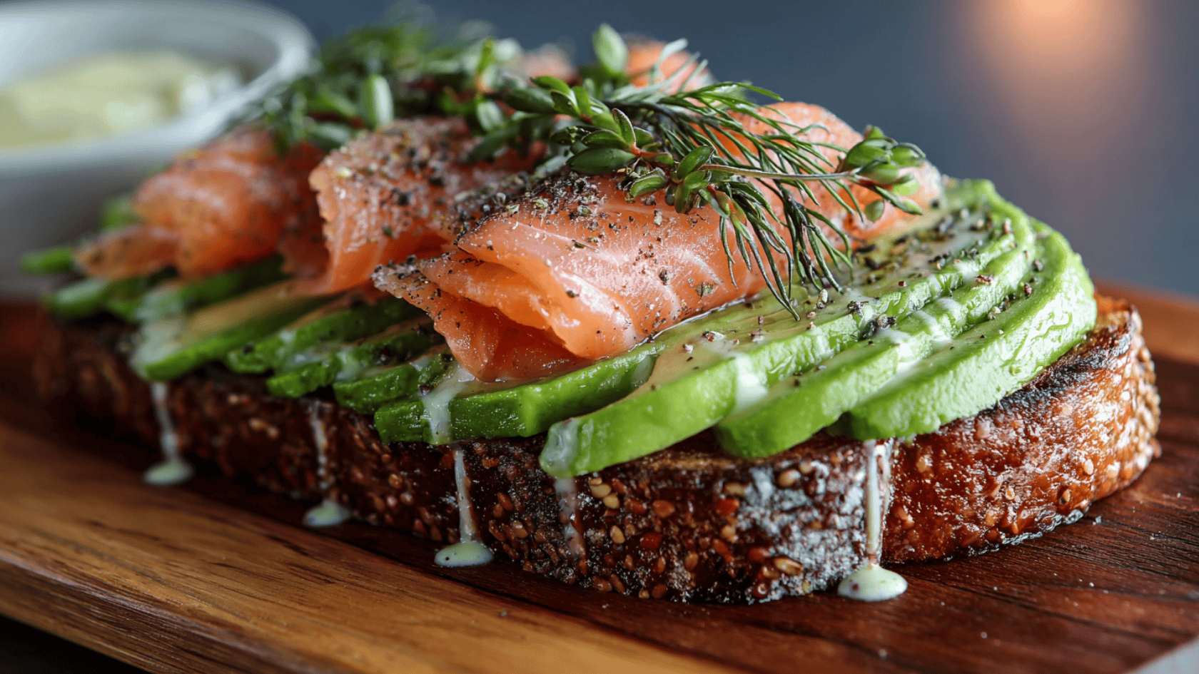 A dish displaying ripe avocado, a portion of salmon, and a sprinkle of herbs for garnish
