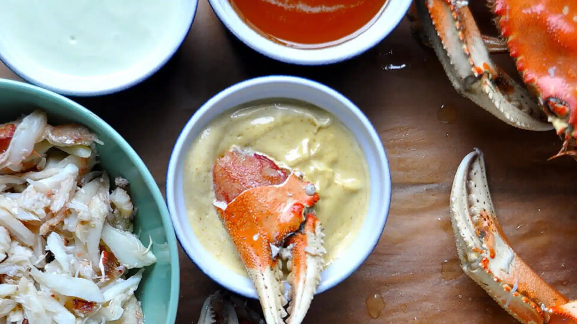 Cooked crab claws and shredded crab meat served with three dipping sauce on a brown surface