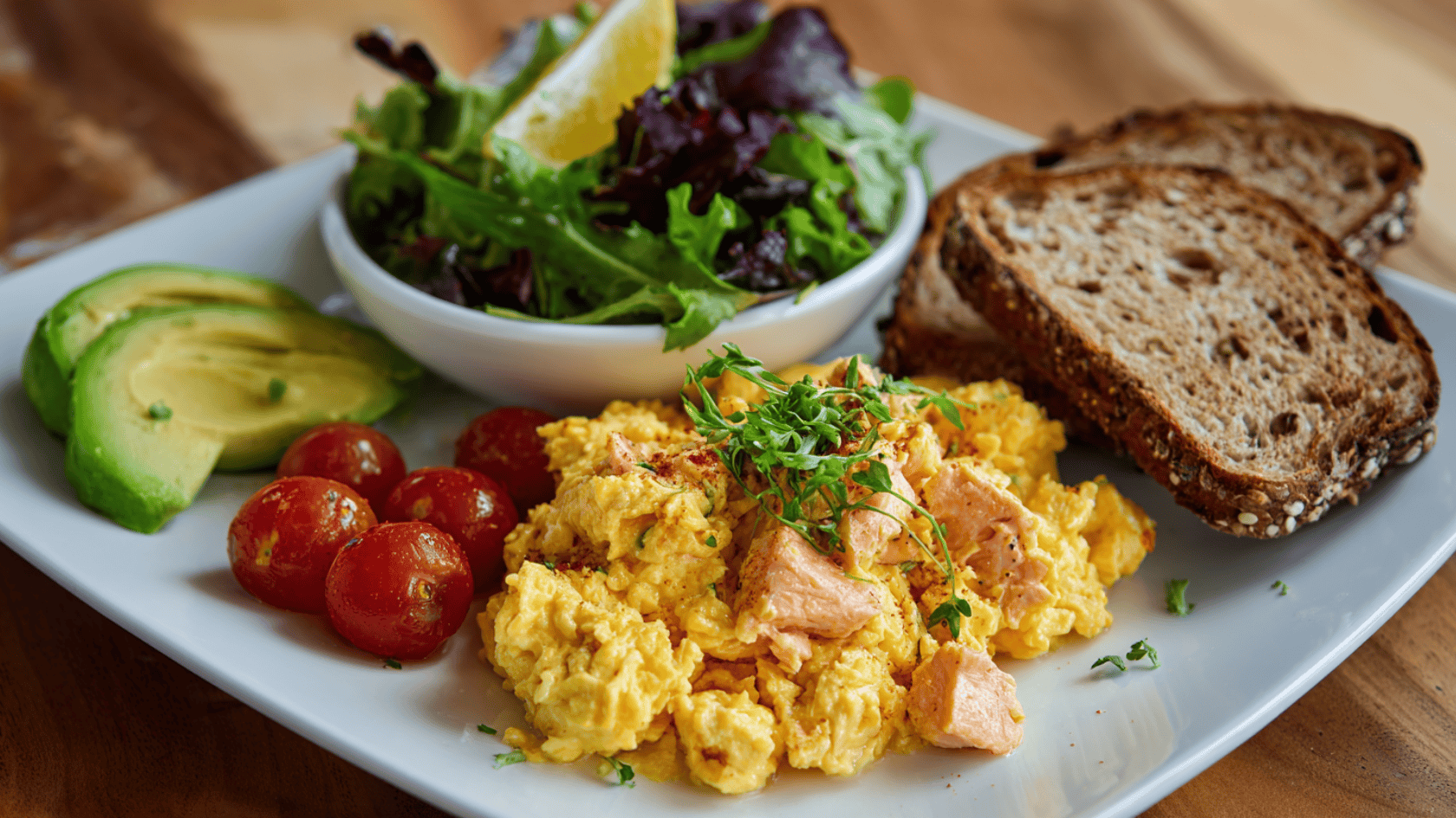 Salmon and egg scramble with avocado, bread, and salad on a white plate