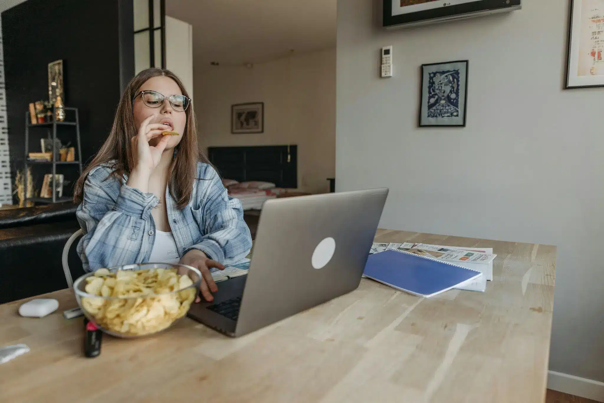 Woman eating chips at desk with laptop in cozy home office setting