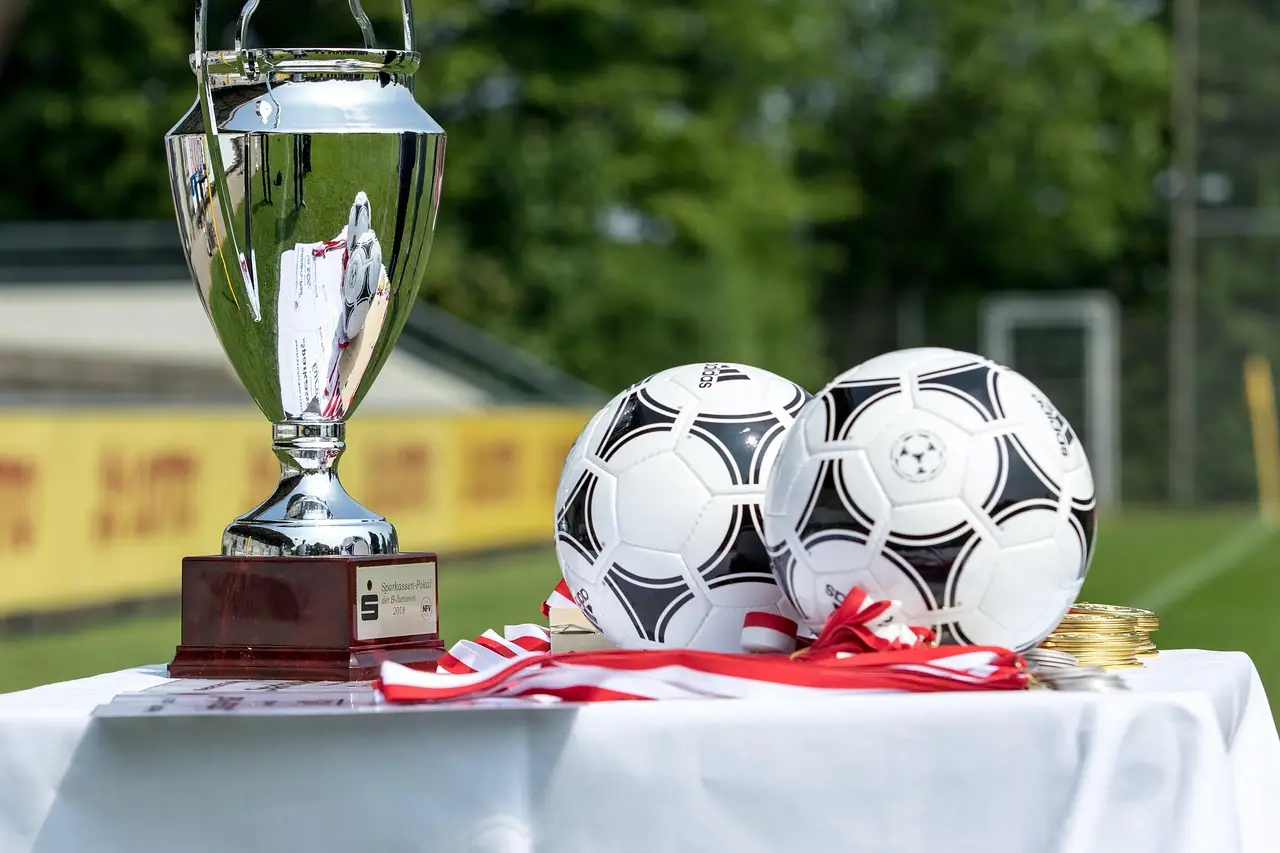 Silver trophy and soccer balls on table with medals in outdoor setting