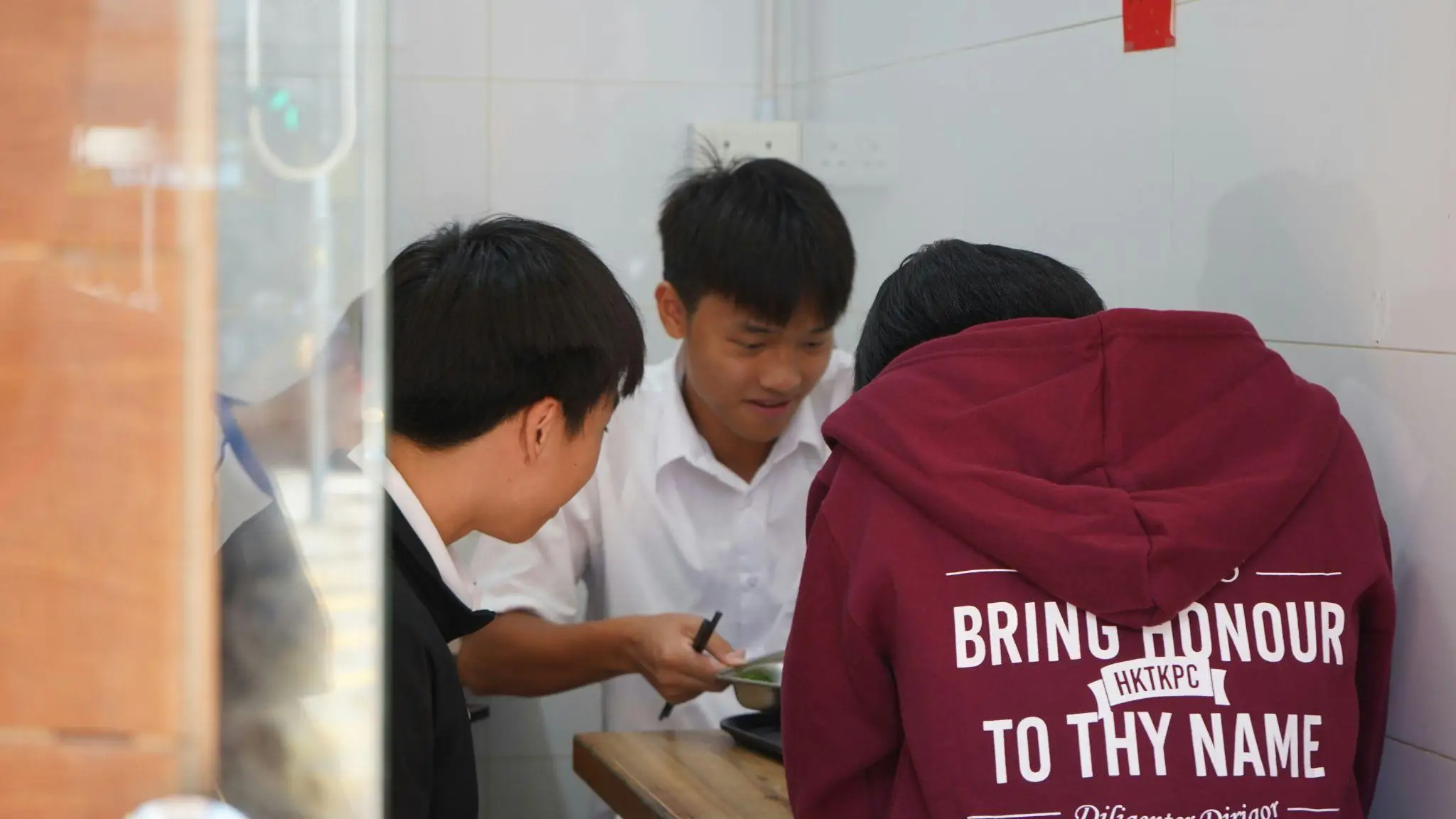 Three young people gathered at a wooden table in a small, tiled room