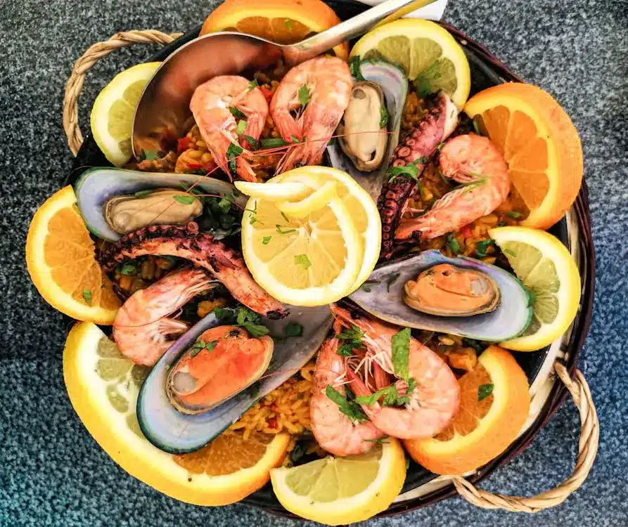 Seafood paella with mussels, shrimp, and lemon slices on a woven basket plate