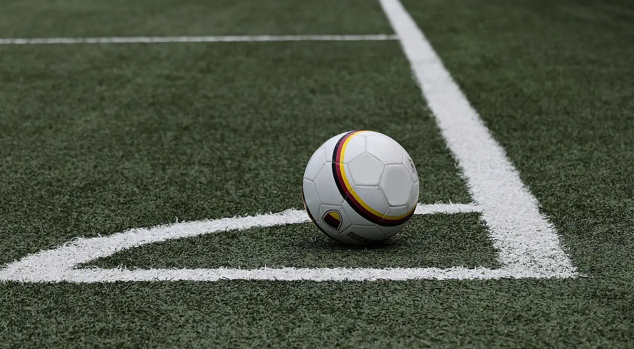 Soccer ball on green turf near white corner line in sports field