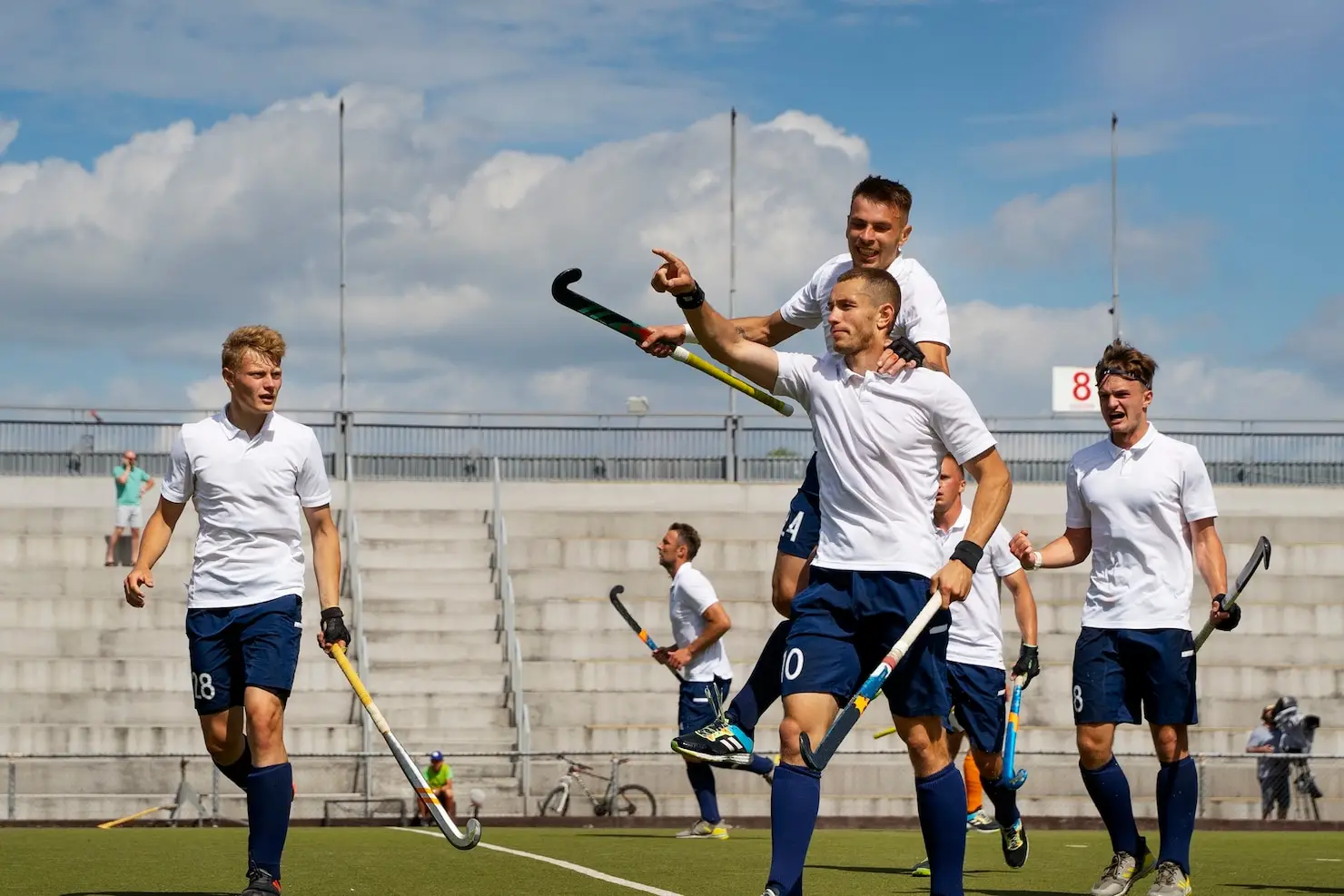 Field hockey players celebrating a goal on outdoor pitch under clear blue sky