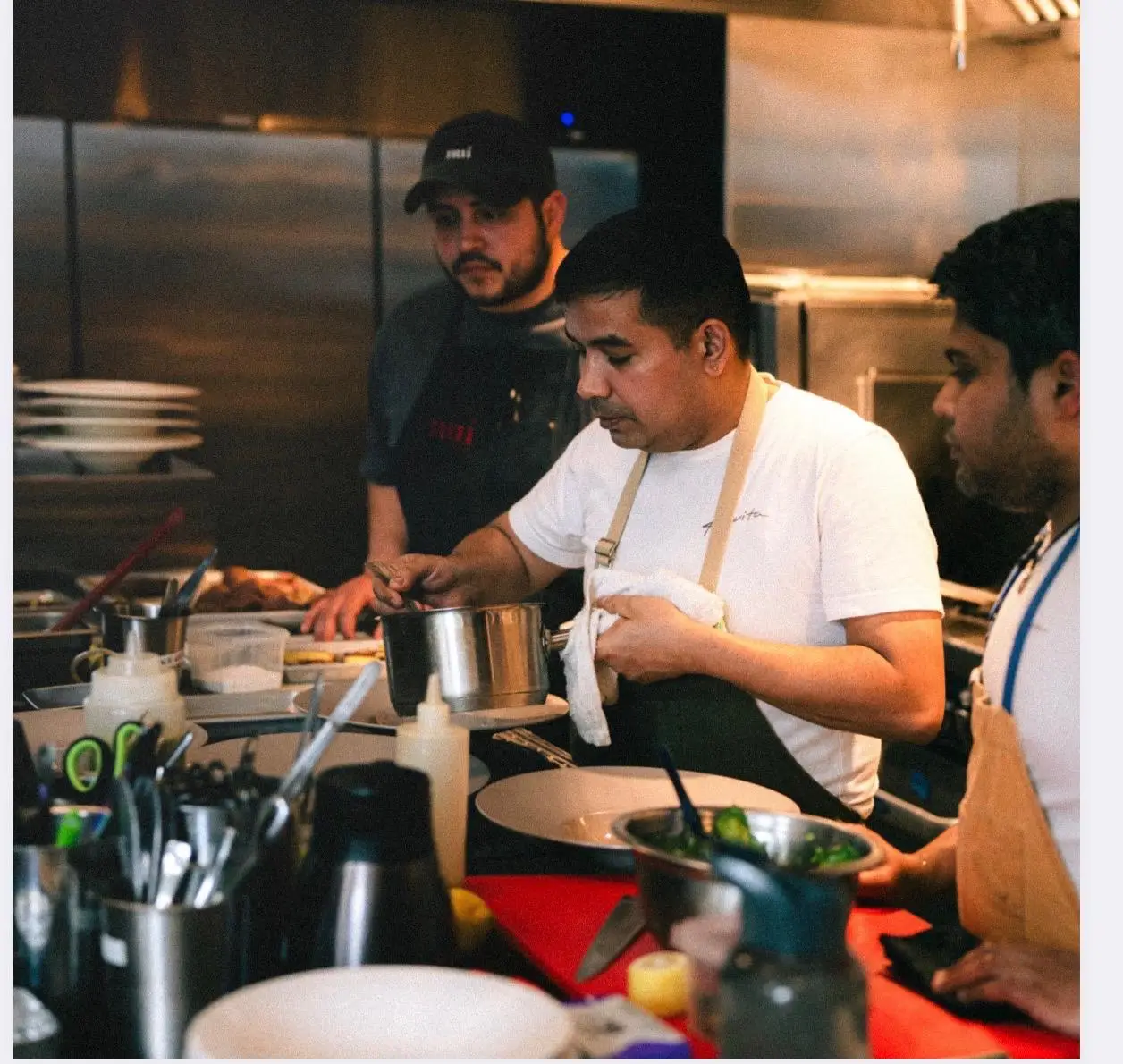 Chefs preparing food in a professional kitchen with stainless steel counters and industrial lighting