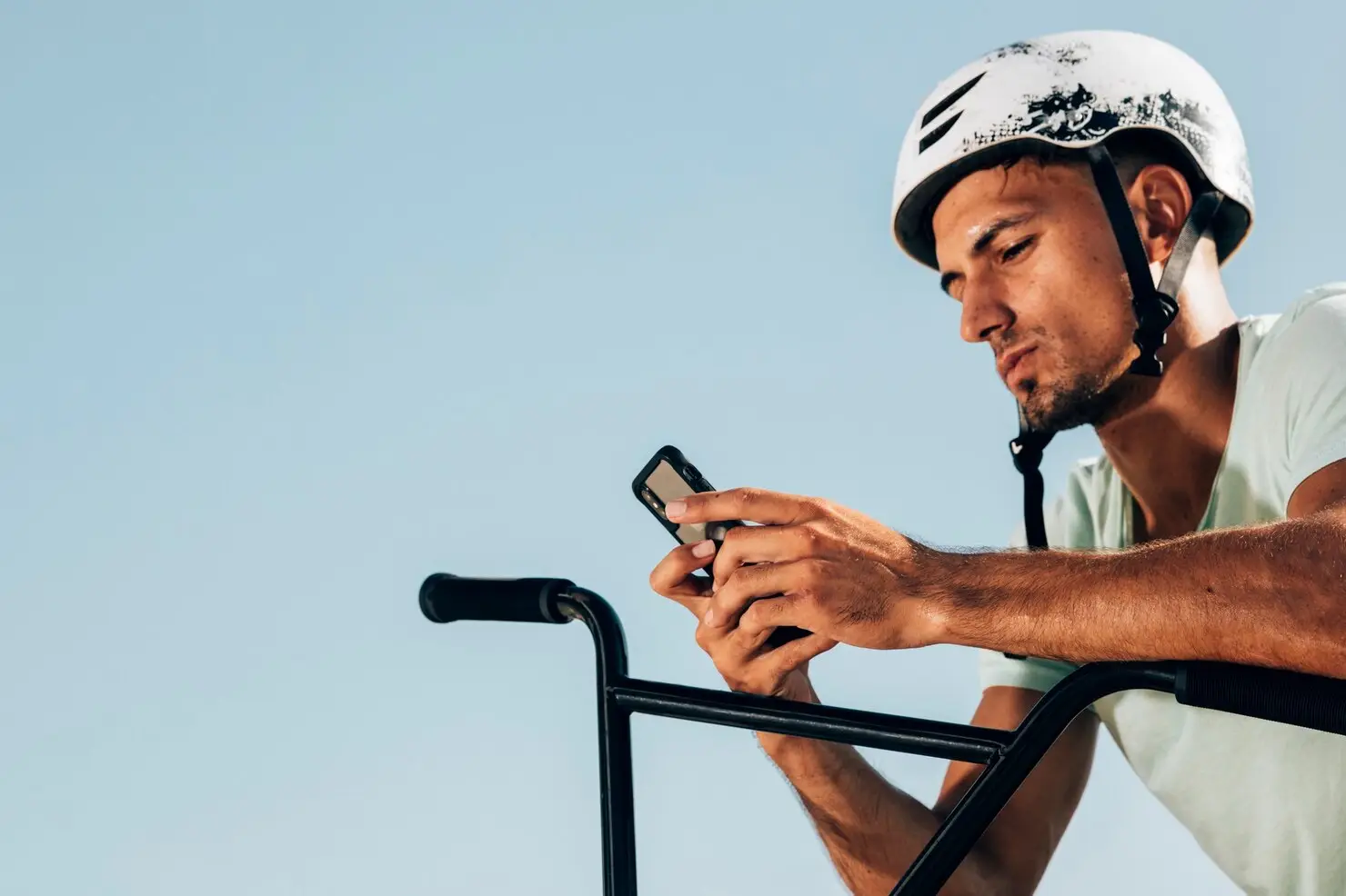 Man wearing helmet on bicycle using smartphone in bright outdoor setting