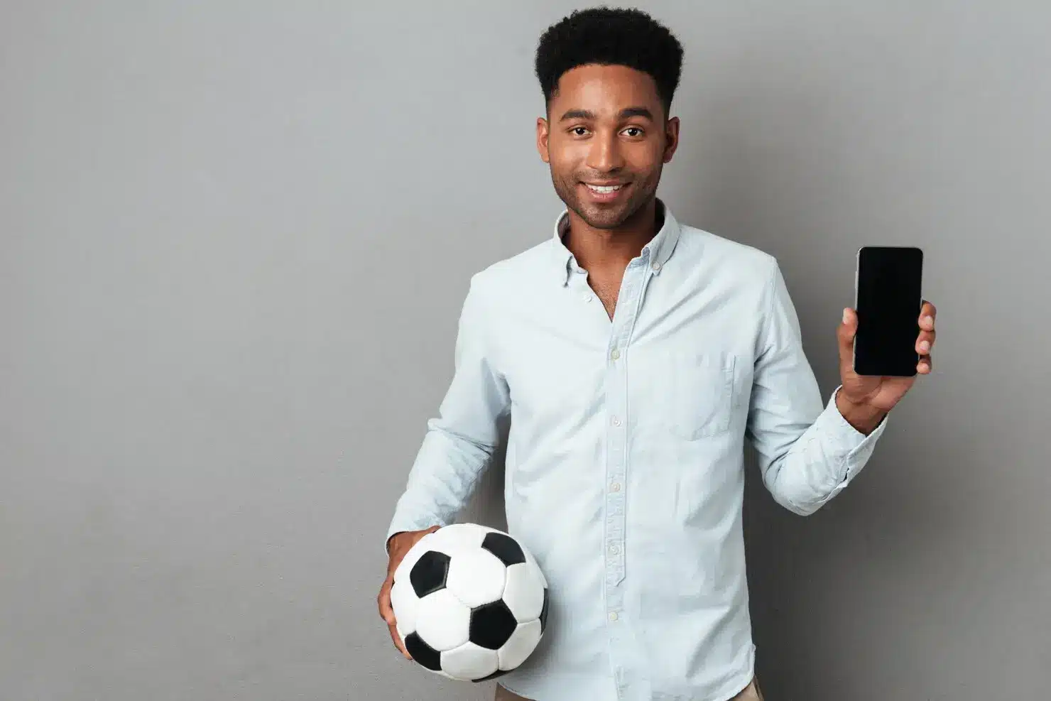 Man holding a soccer ball and smartphone against gray background