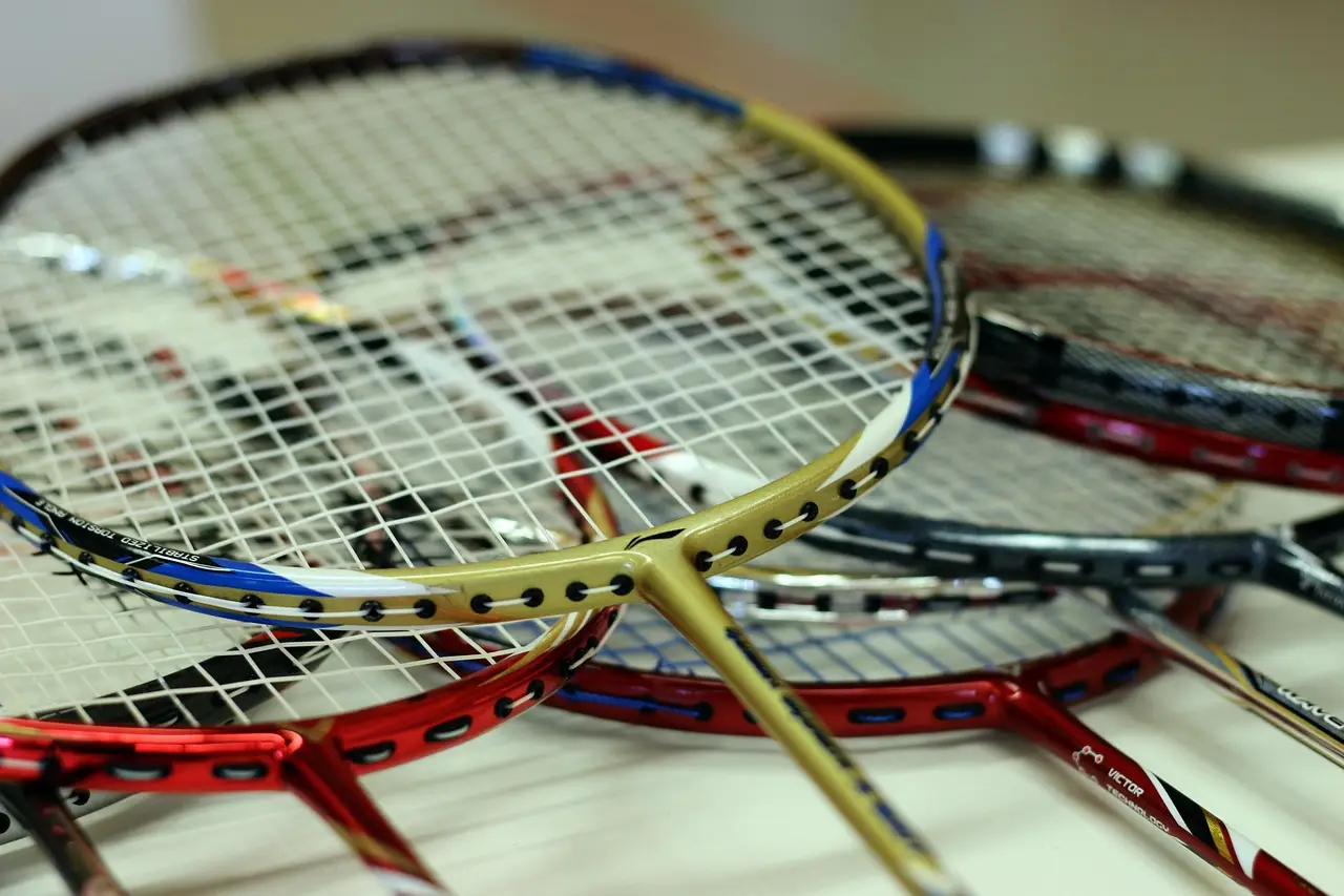 Multiple badminton rackets with varied colored frames stacked on white table surface