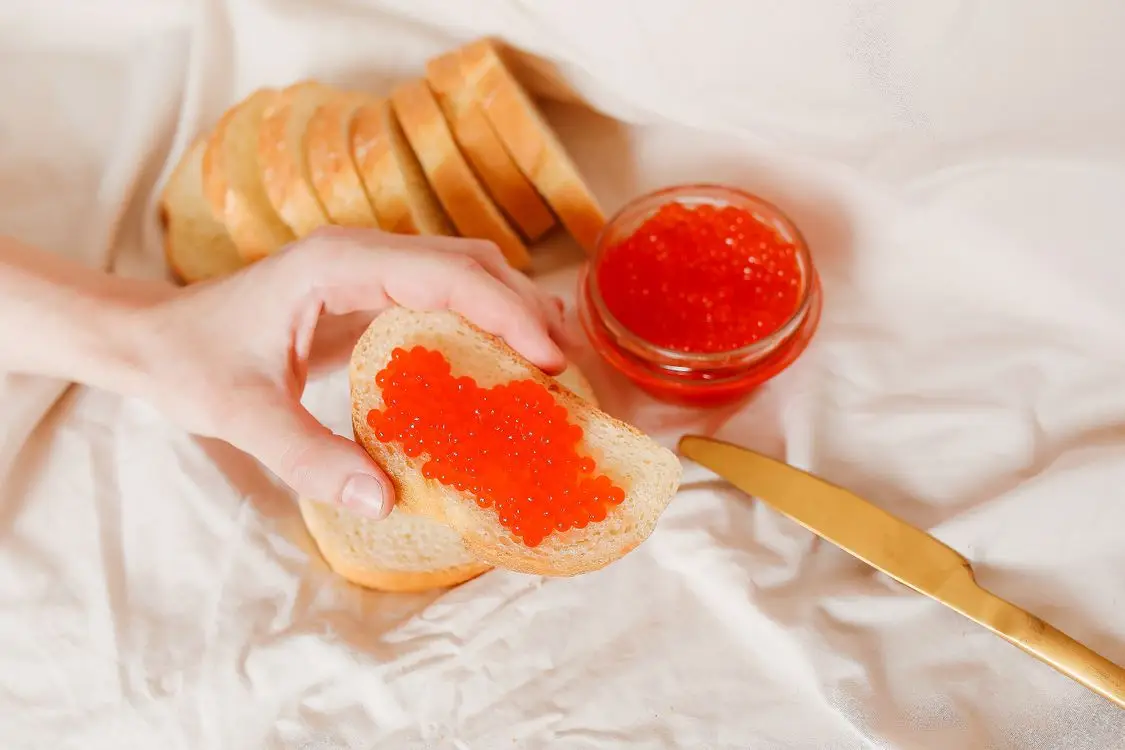 Hand holding slice of bread with red caviar over white cloth background