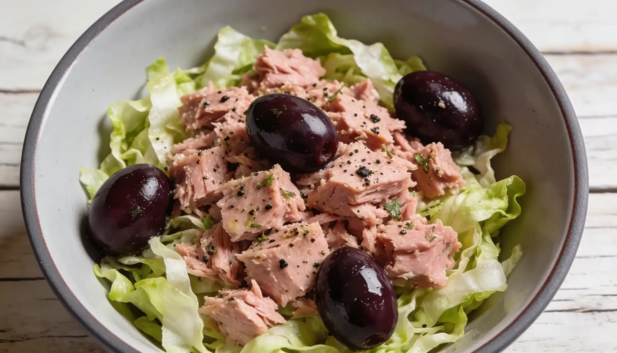 Tuna salad with Kalamata olives on a bed of lettuce in a bowl.