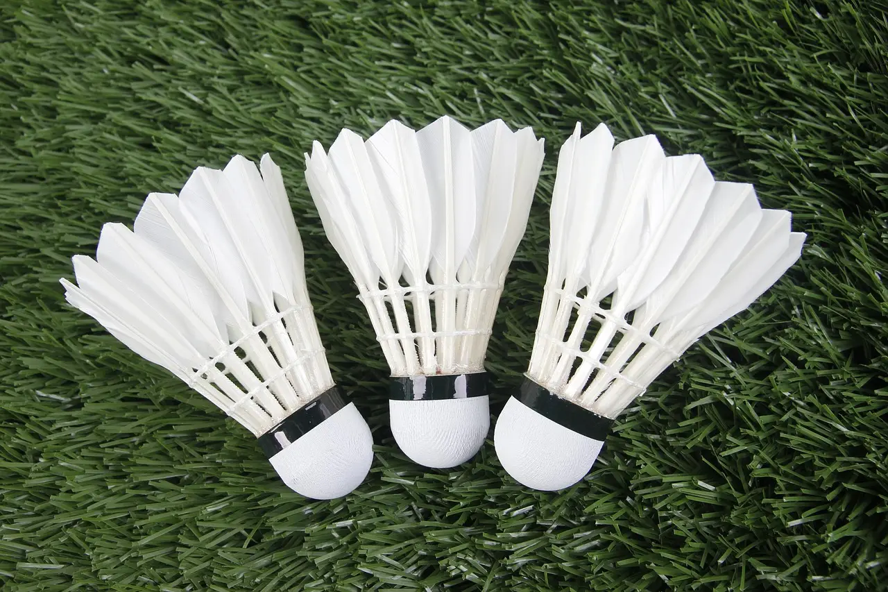 Three white shuttlecocks lying on green artificial grass