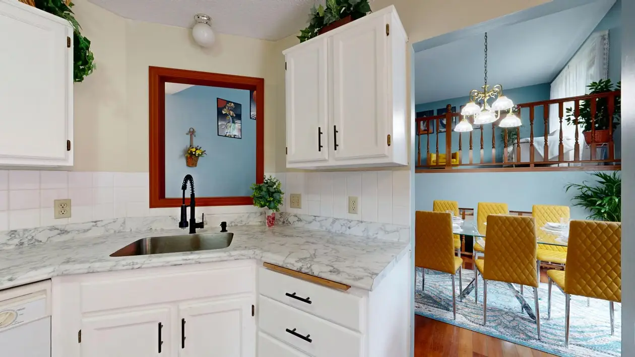 White kitchen with marble countertops and view into dining room with yellow chairs and blue walls