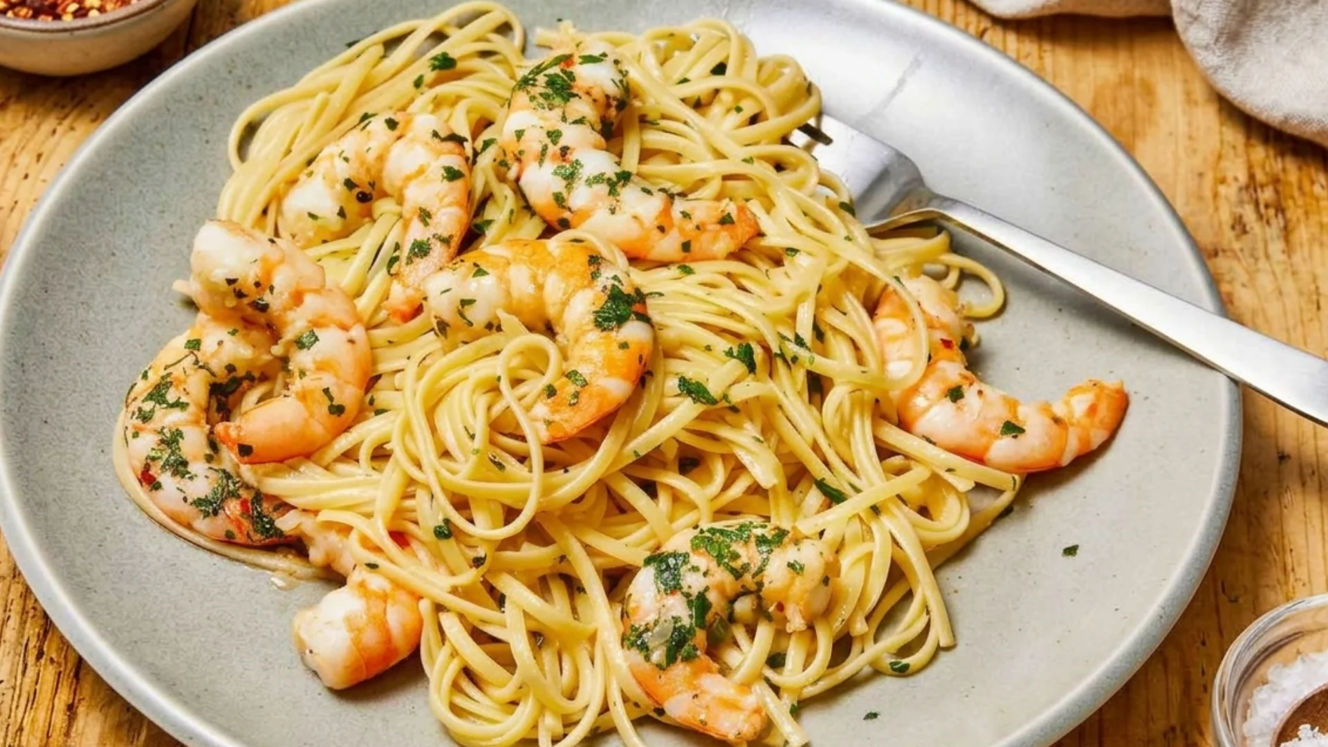 Linguine pasta with shrimp and parsley, served on a gray plate with a fork.