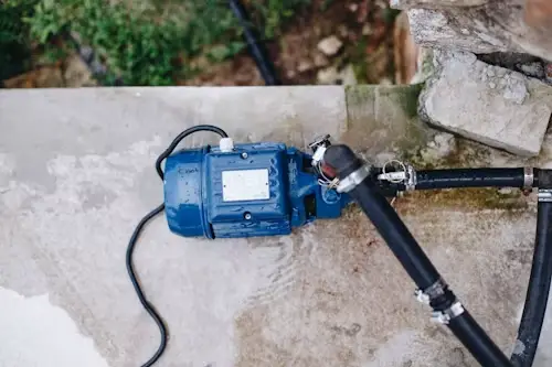 Blue water pump with black hoses on concrete surface outdoors near stone wall