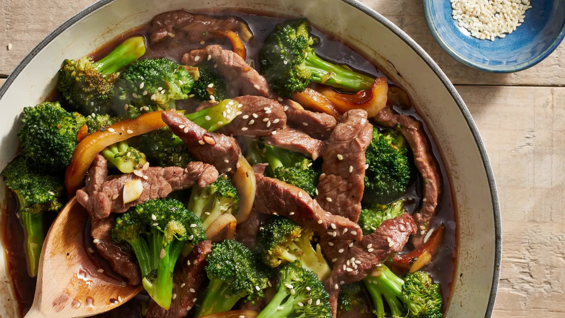 A bowl containing beef and broccoli, with a wooden spoon placed next to it for easy serving.