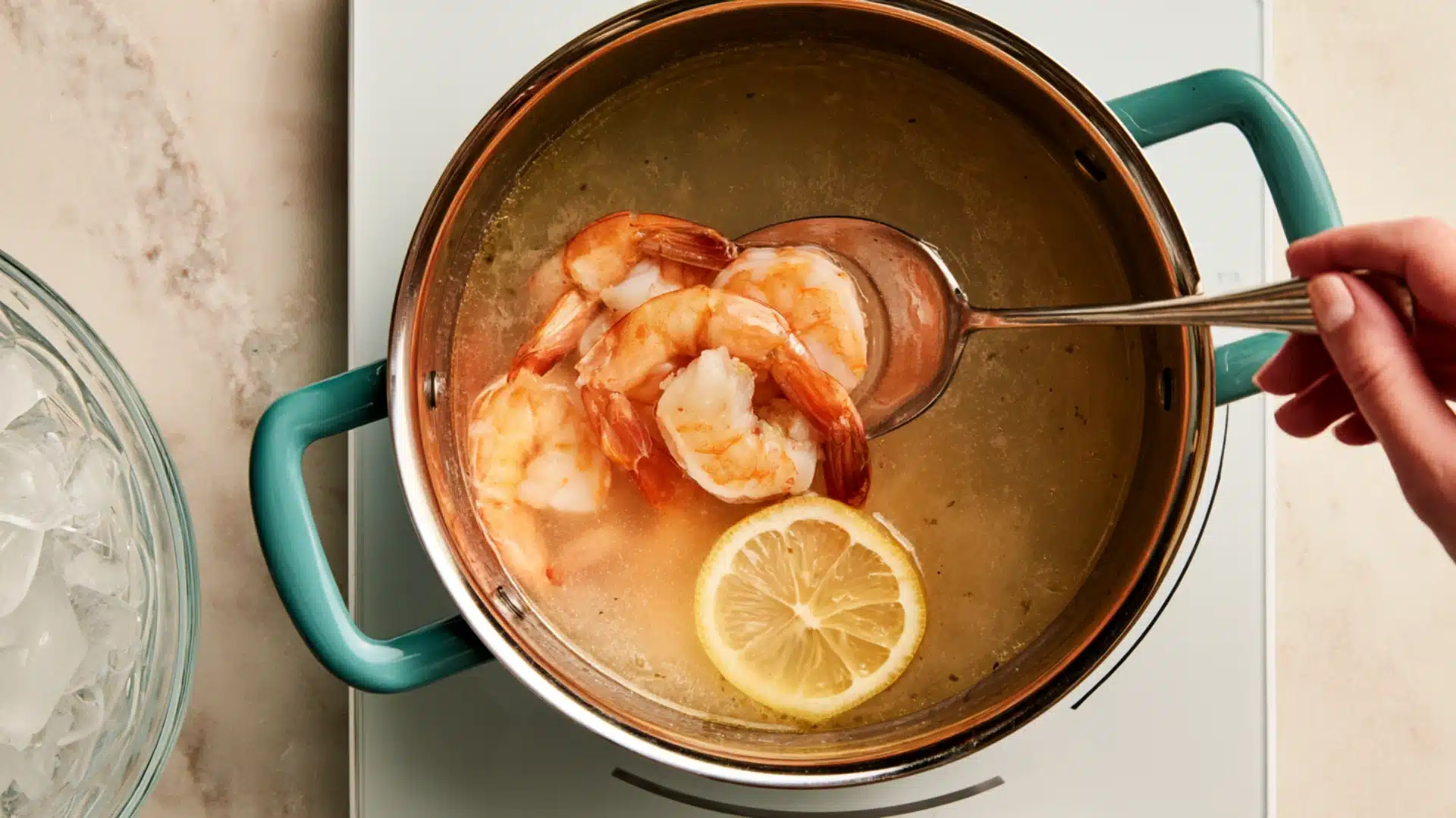 Cooked shrimp being lifted from a pot of poaching liquid with a slotted spoon.