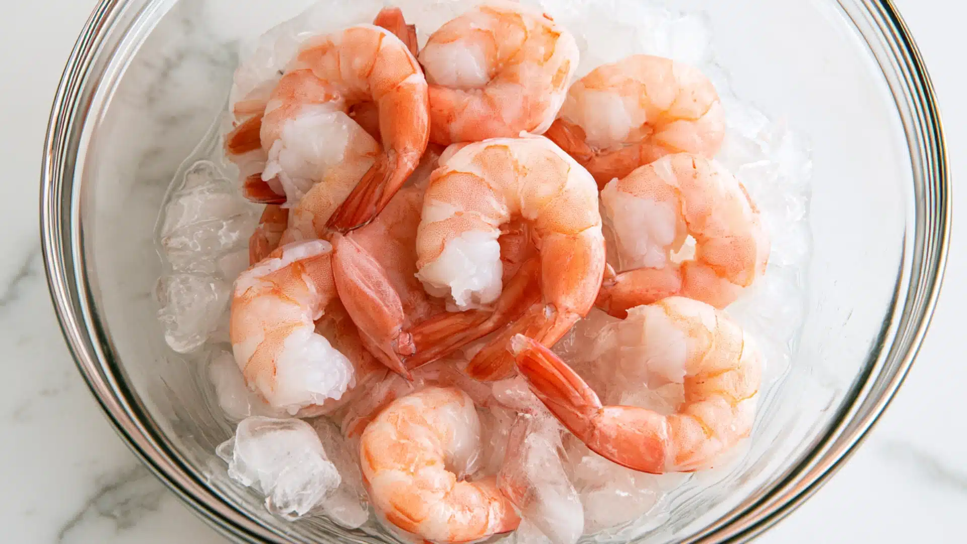 Cooked shrimp cooling in a glass bowl filled with ice water.