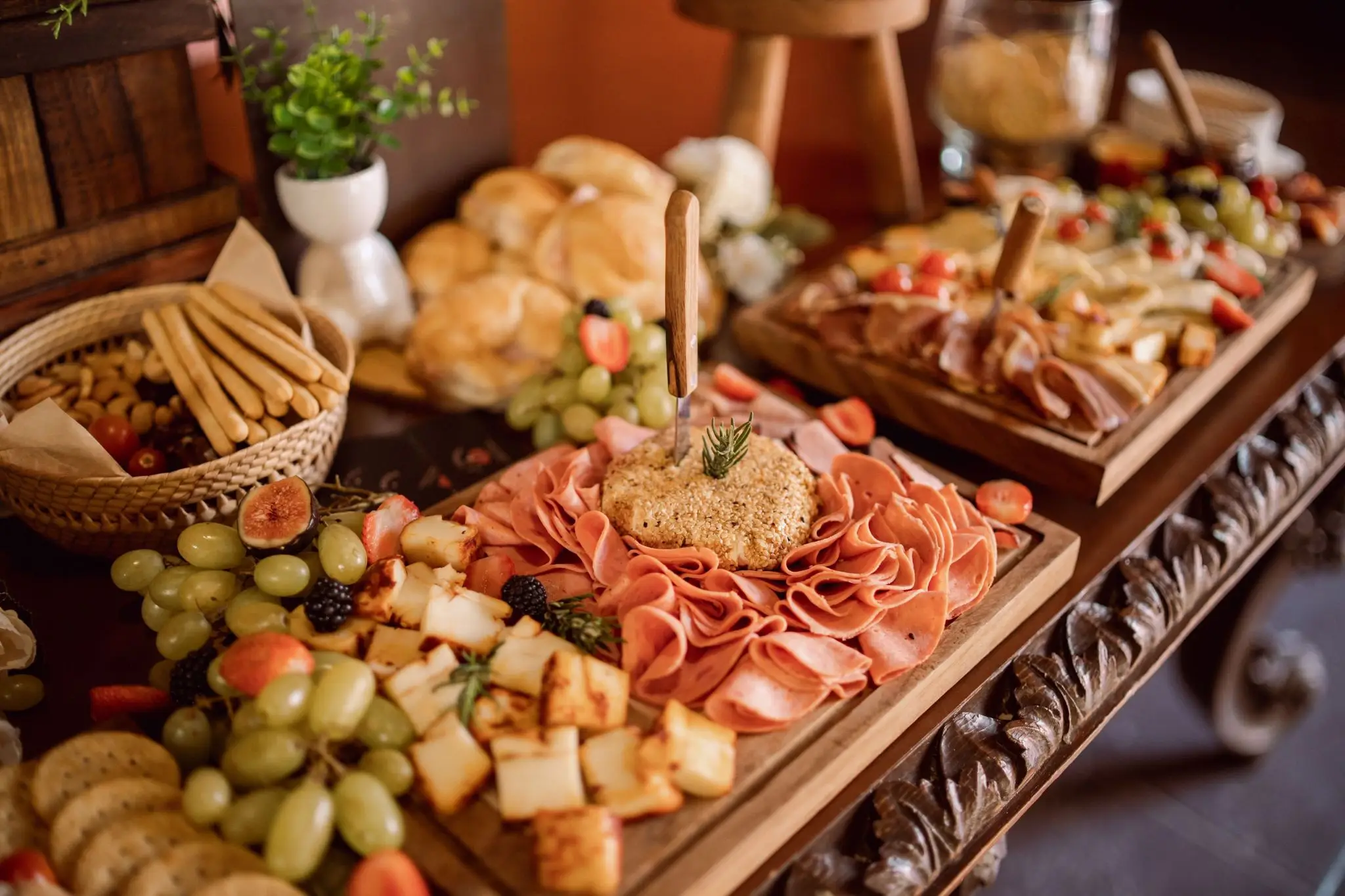 Charcuterie board with assorted meats, cheese, fruits, and breadsticks in a rustic indoor setting