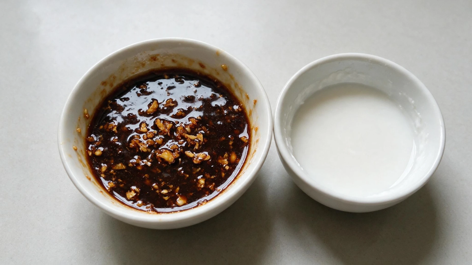 A wooden table featuring two bowls of soy sauce and cornstarch slurry respectively.