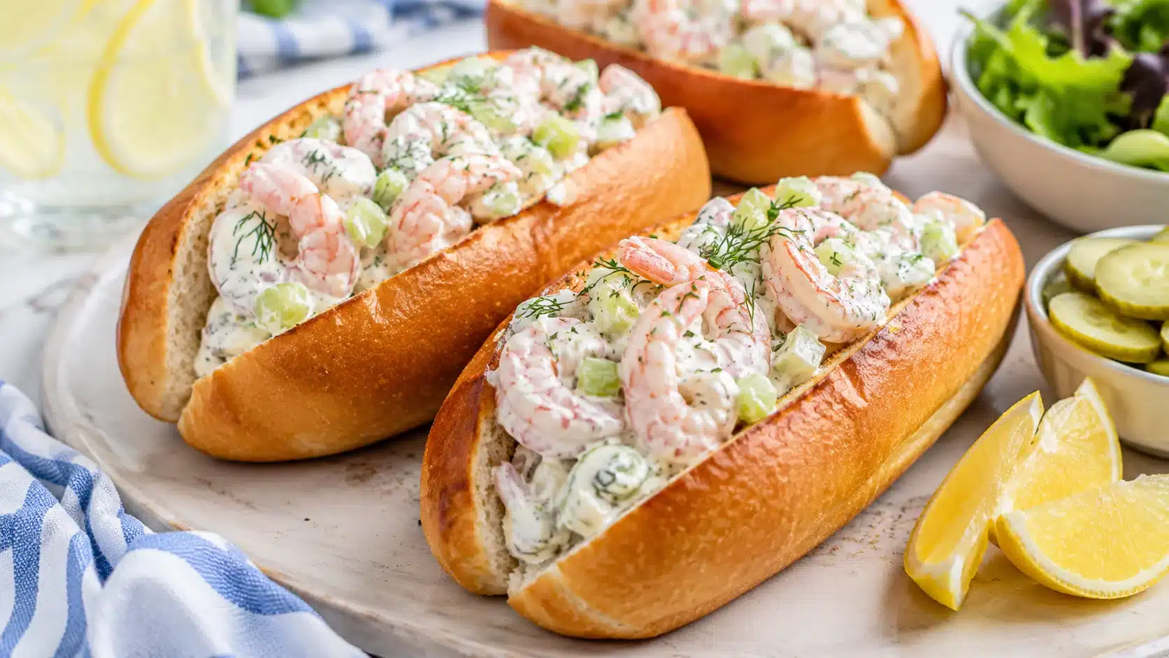 lighter greek yogurt shrimp rolls with celery, dill, lemon wedges, pickles, and toasted split-top buns