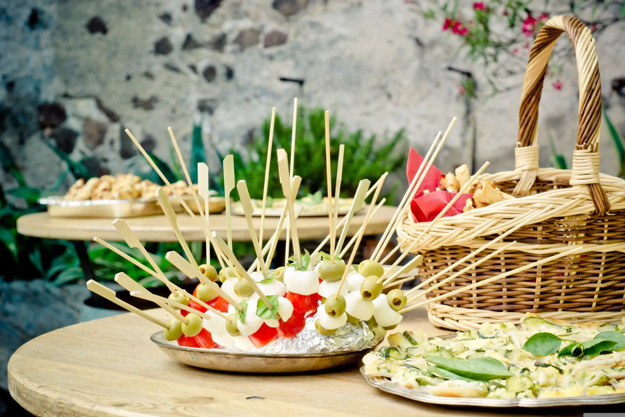Skewered olives, mozzarella, tomatoes on plate with wicker basket and outdoor stone wall background