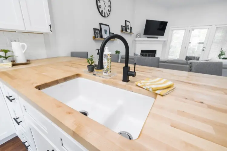 Modern kitchen with light wood countertops, black faucet, and decorative plants in bright setting