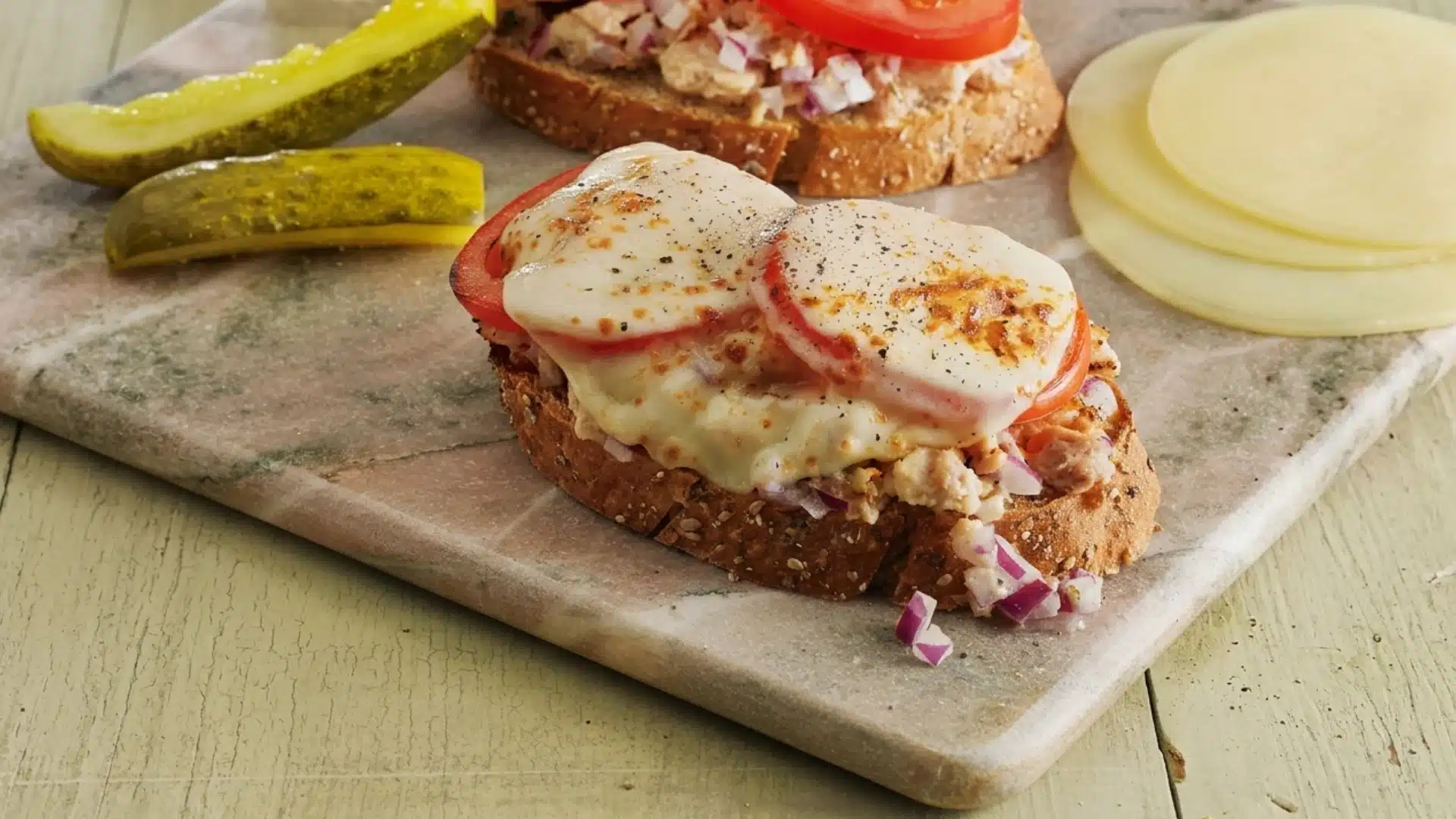 Open face tuna melt with tomato and melted cheese on toasted bread.
