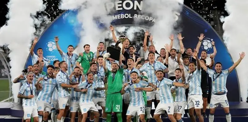 Soccer team celebrating with trophy on stage surrounded by smoke and lights