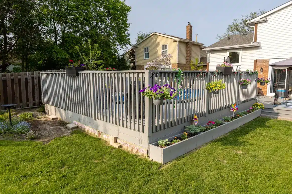 Wooden deck with hanging flower pots in suburban backyard surrounded by grass and trees