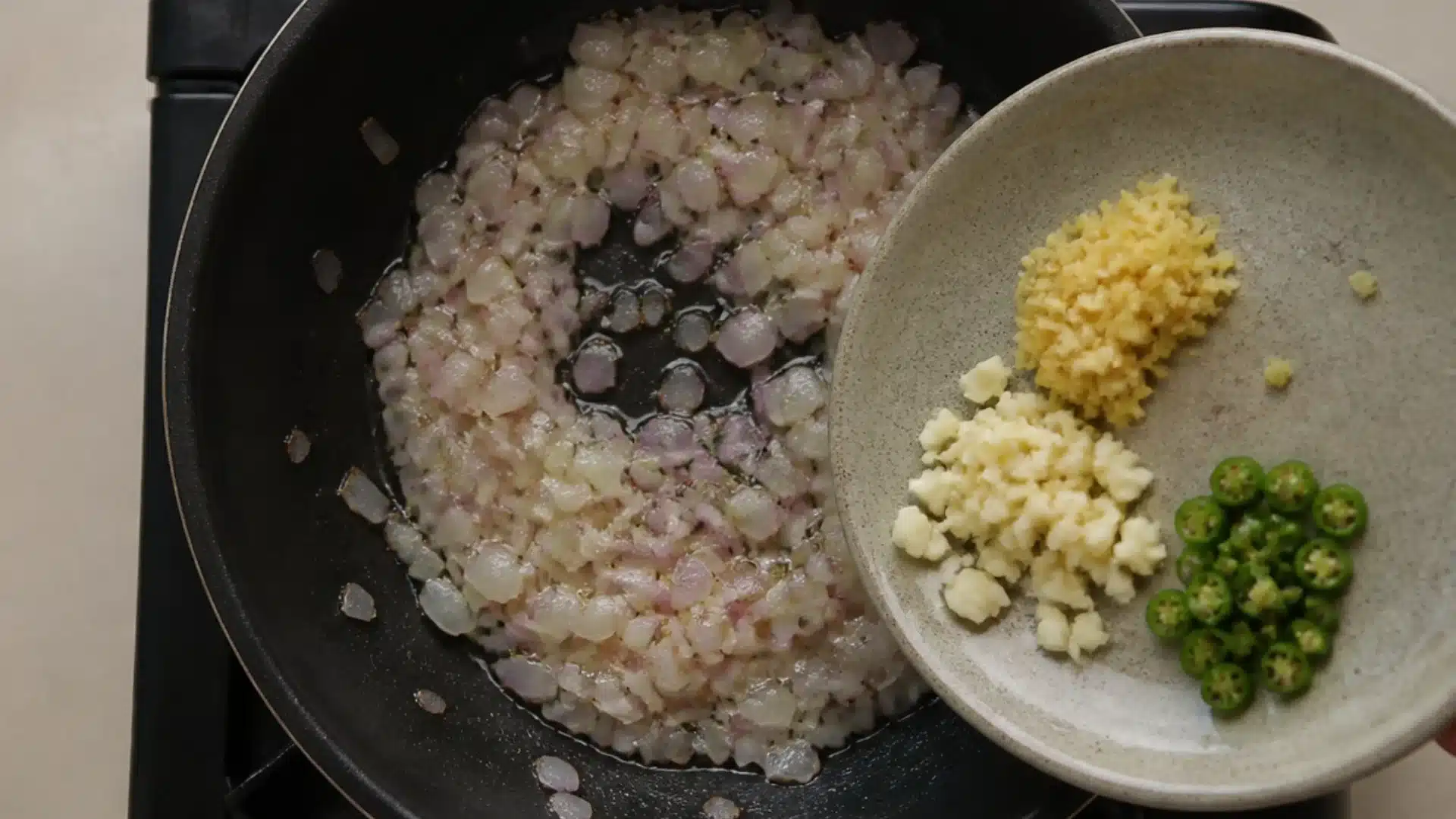 Chopped onions cooking with ginger garlic and green chilies in a pan