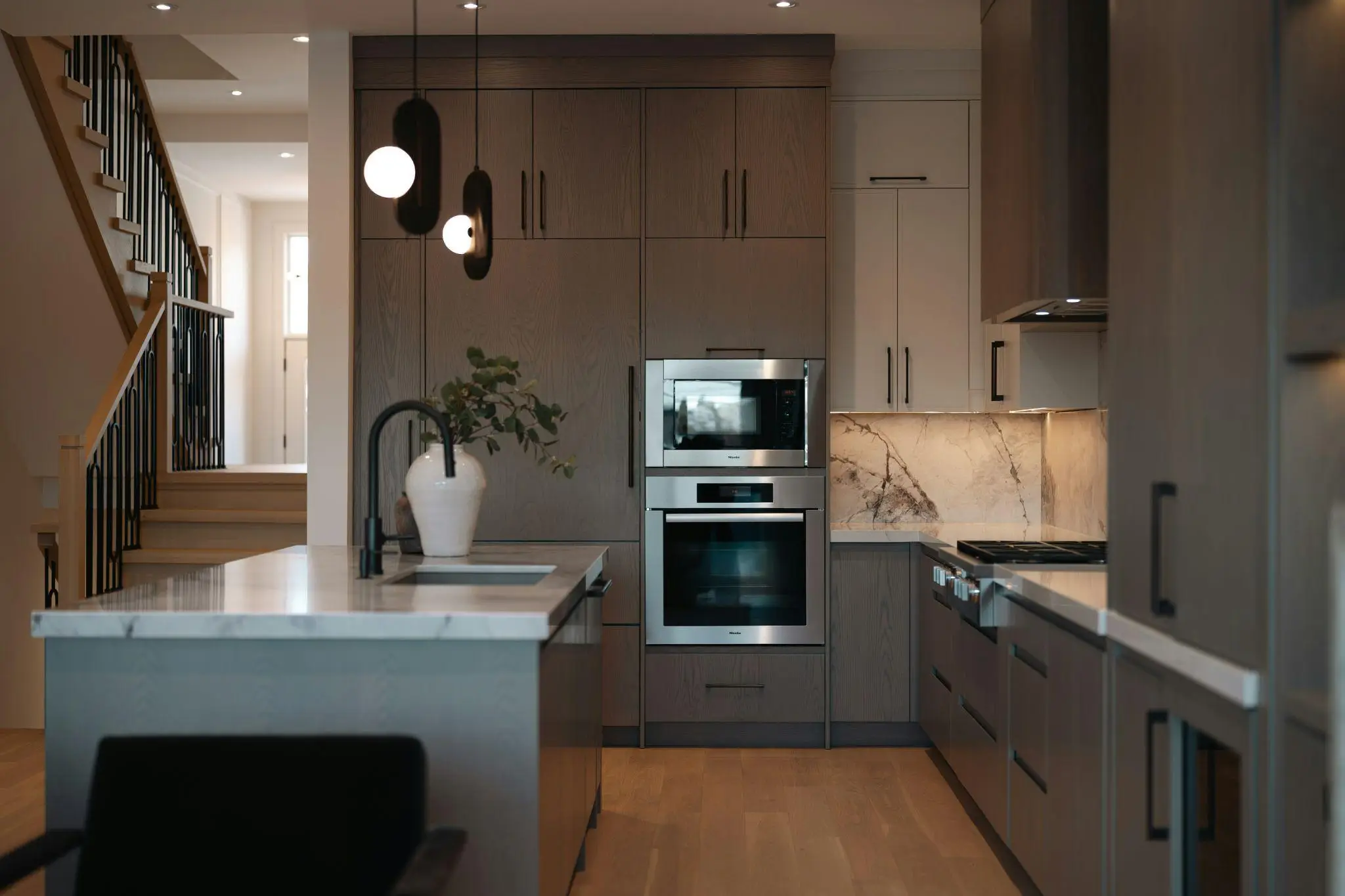 Modern kitchen with dark wood cabinets, stainless steel appliances, marble countertops, and pendant lighting