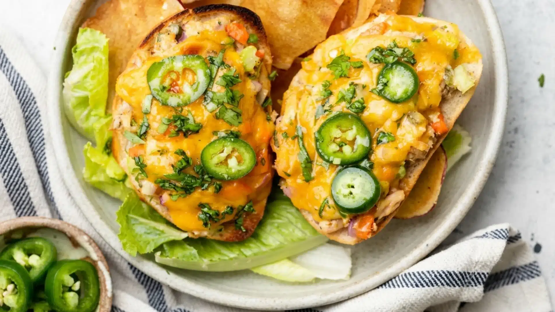 Open face tuna melts topped with jalapeño slices and melted cheese on lettuce.