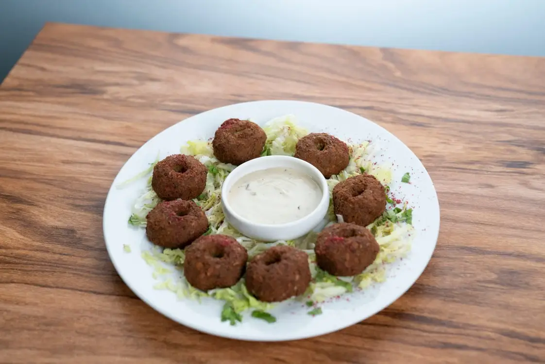 Falafel arranged around creamy dipping sauce on white plate with shredded lettuce