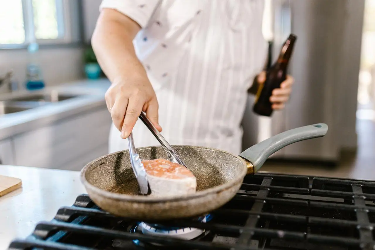 Chef cooking salmon in frying pan on gas stove in kitchen