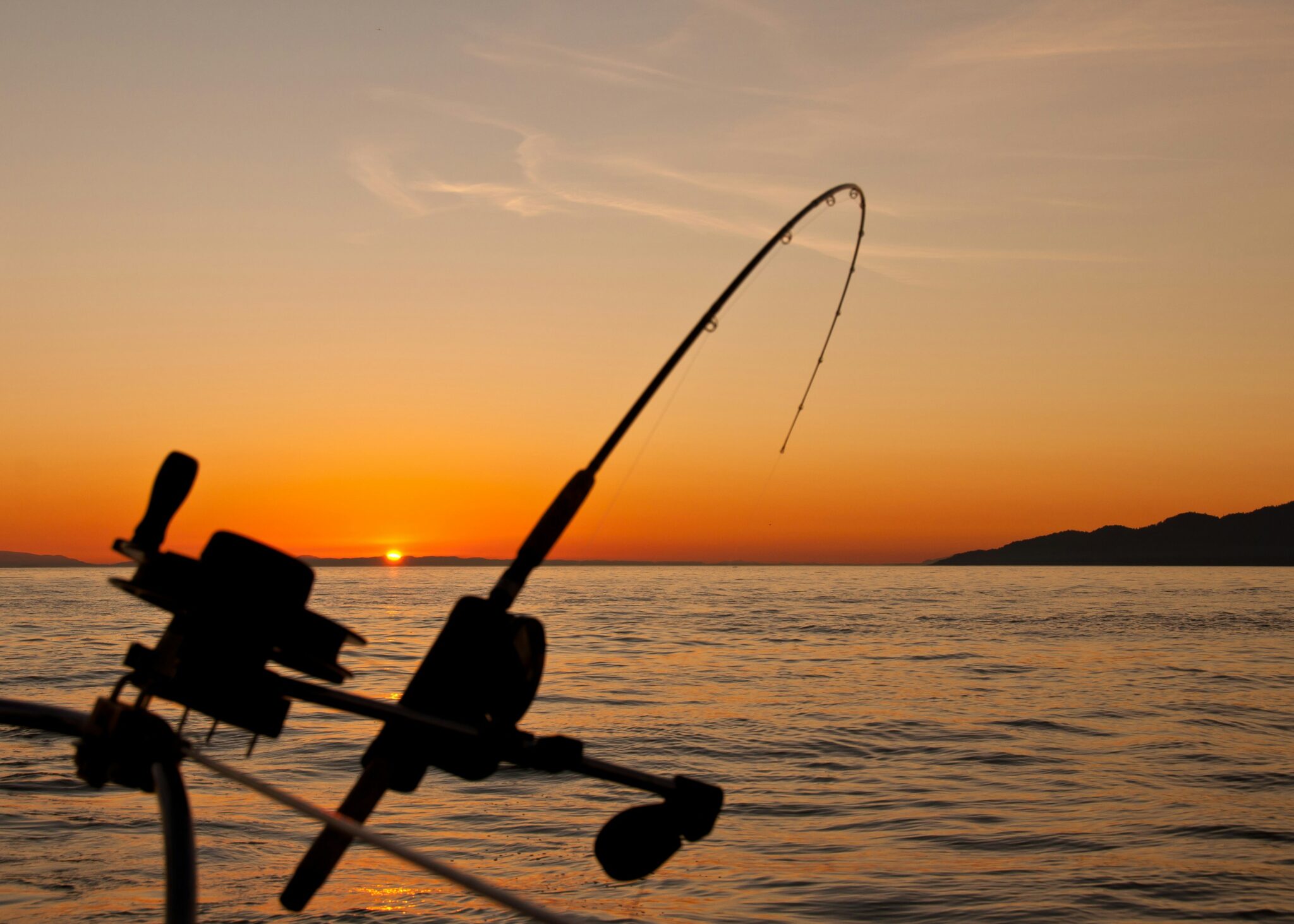 Fishing rod silhouetted against an orange sunset over the ocean waves