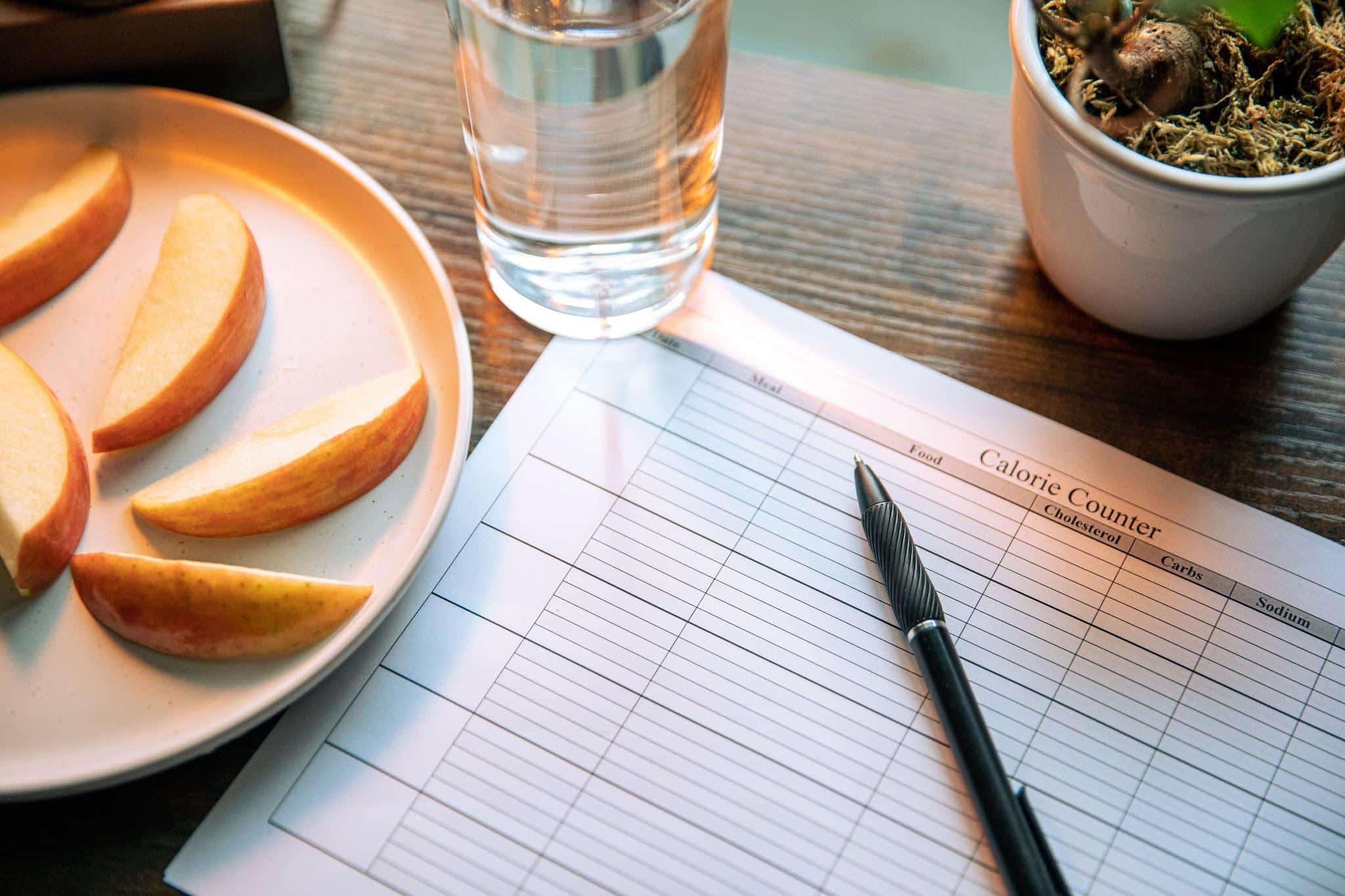 Apple slices on plate with glass of water and calorie counter sheet on wooden table